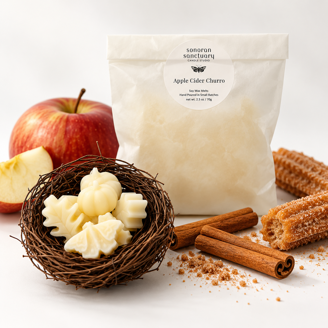 Sonoran Sanctuary Apple Cider Churro wax melts in branded packaging with botanical-shaped wax melts, fresh apple, cinnamon sticks and cinnamon-sugar churros on a white background